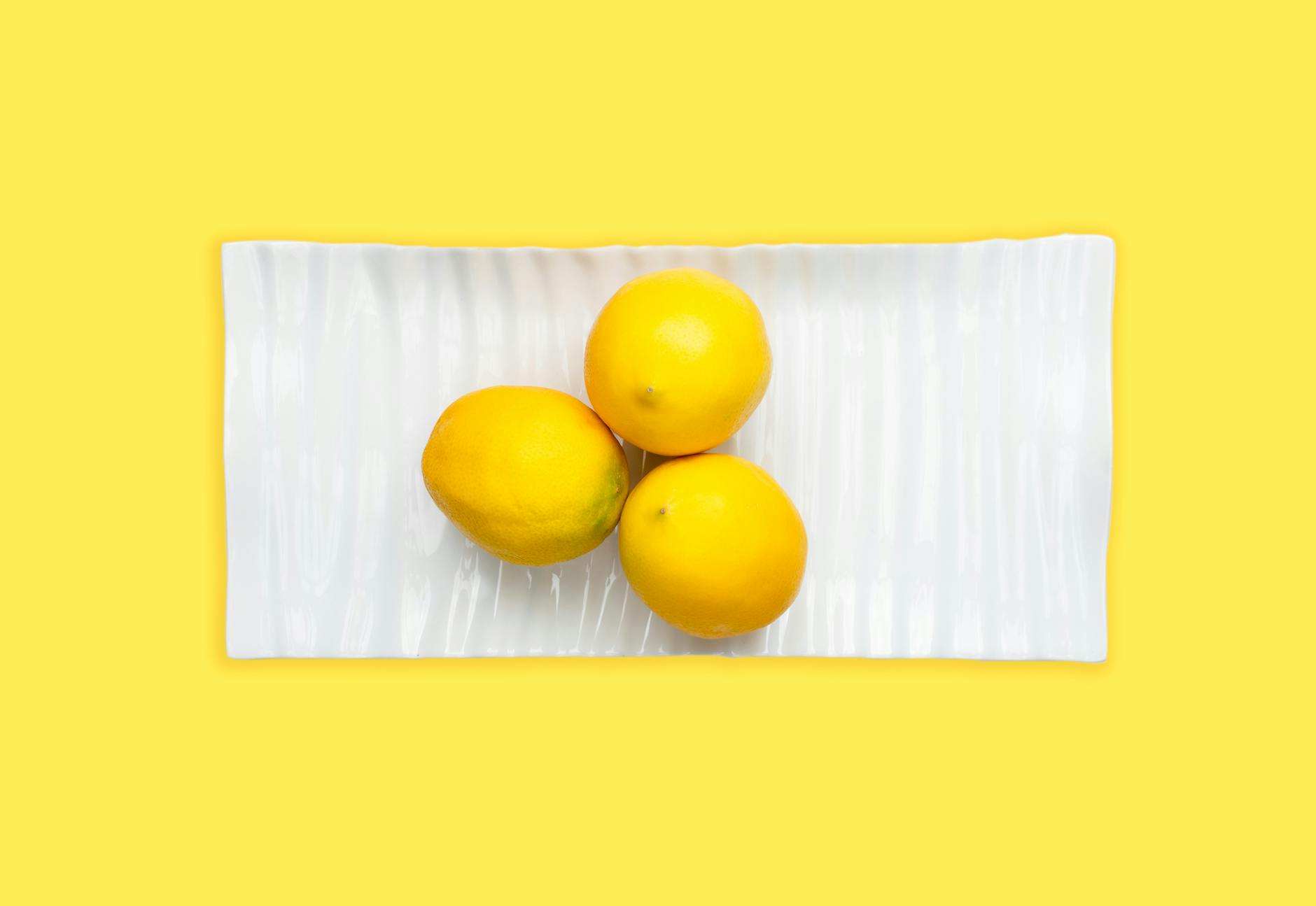 Tres limones frescos en un plato blanco con fondo amarillo vibrante, enfatizando la frescura del vibrador de limón