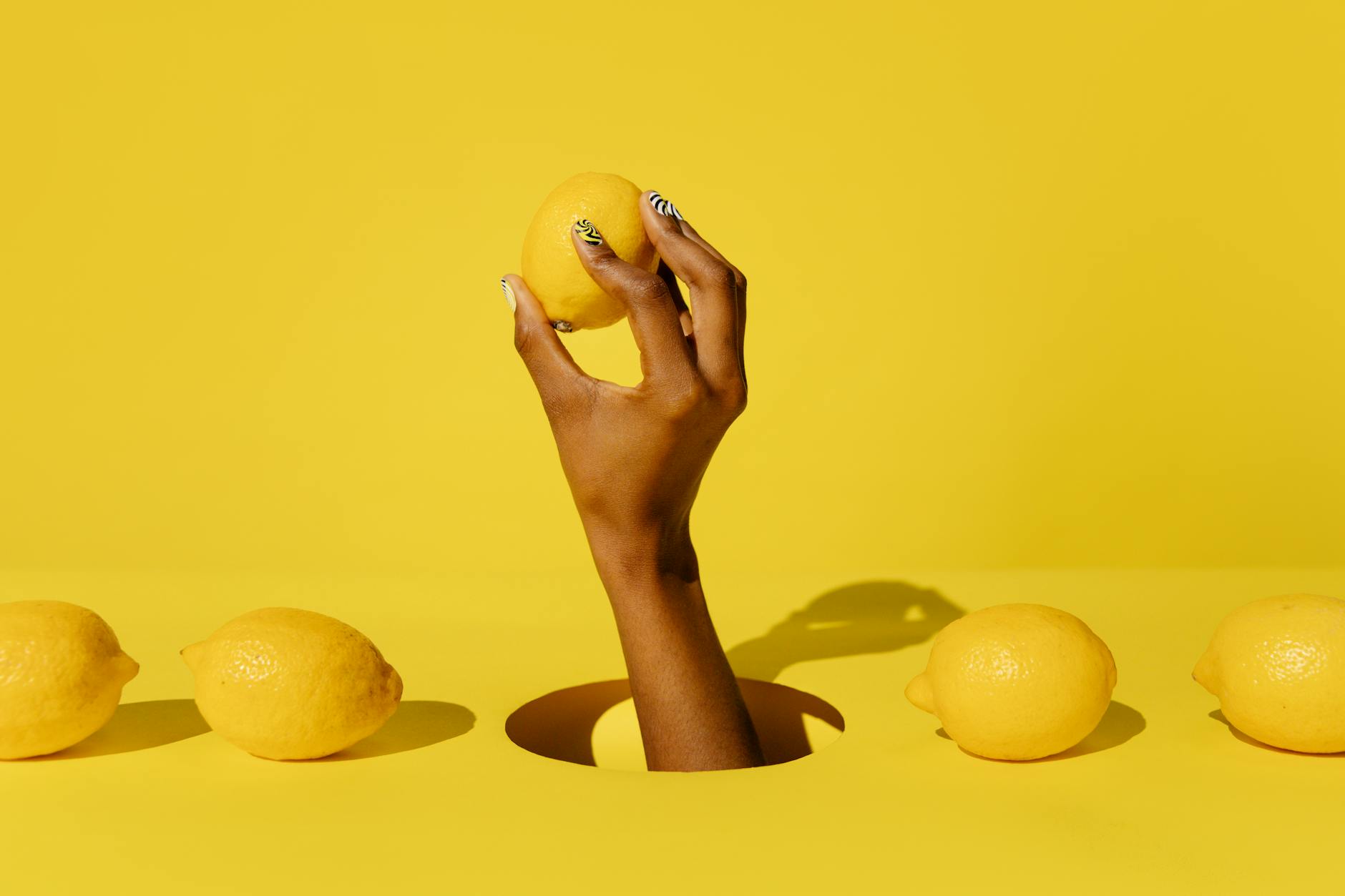 Mano sosteniendo un limón fresco sobre fondo amarillo vibrante