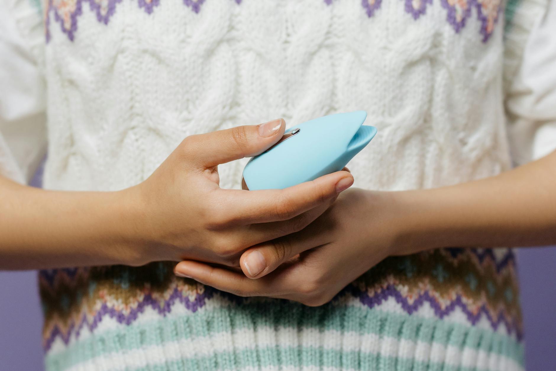 Manos sosteniendo un vibrador personal azul contra un suéter tejido
